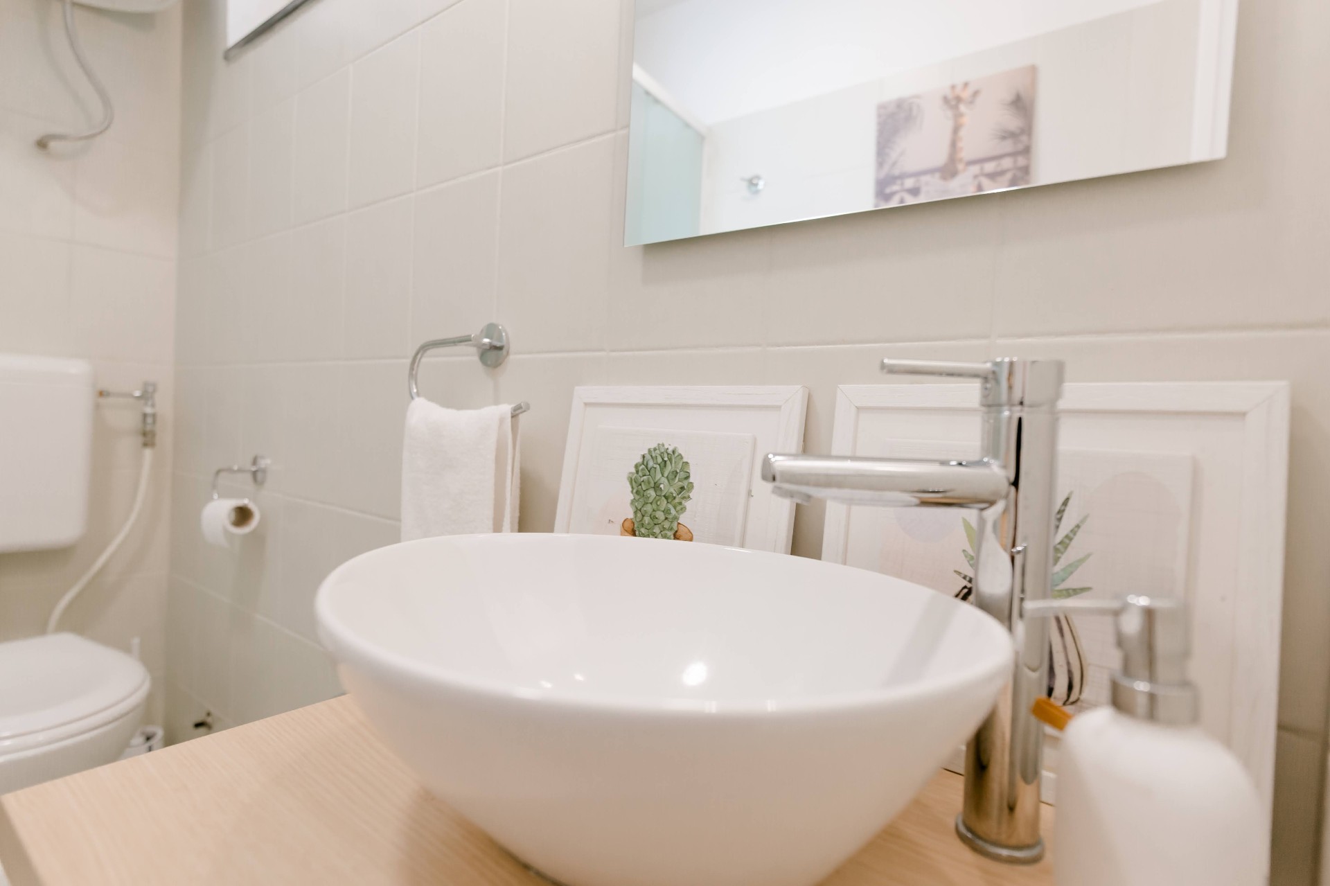 Dettaglio del bagno con lavabo da appoggio in ceramica bianca, miscelatore alto cromato e specchio orizzontale