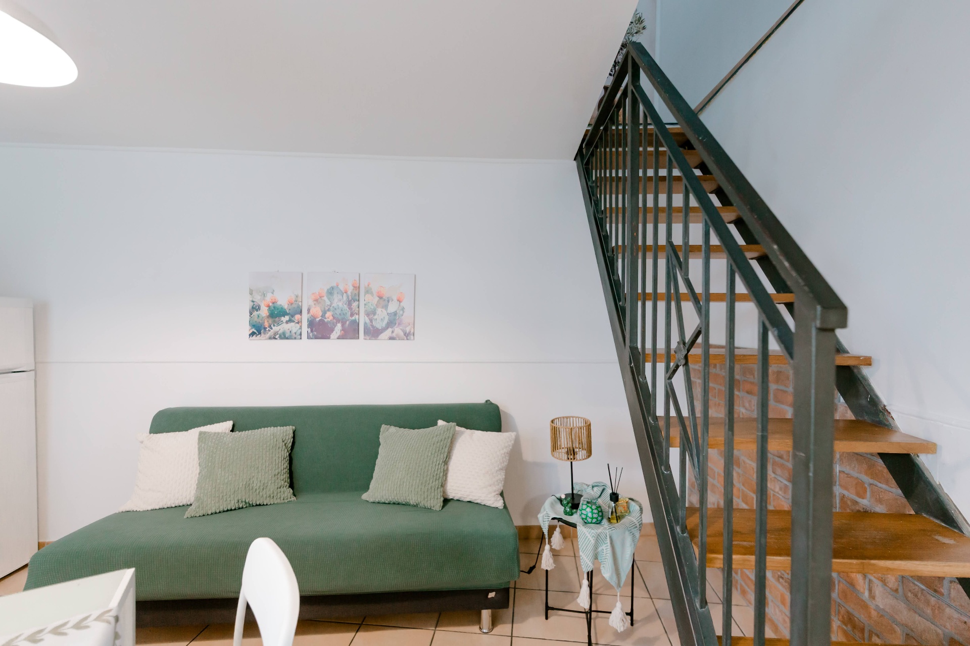 Zona giorno open space di Bedda Matri con divano verde salvia, cuscini coordinati e parete decorativa in mattoni a vista accanto alla scala interna